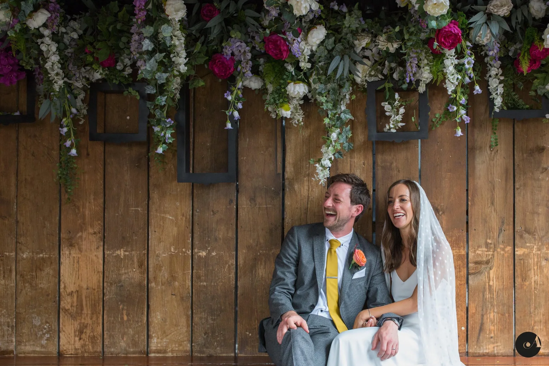 Anna and Sean laughing together beneath a wall of flowers