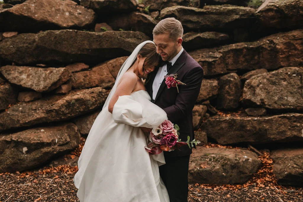 Chloe and John holding each other beside a stone wall