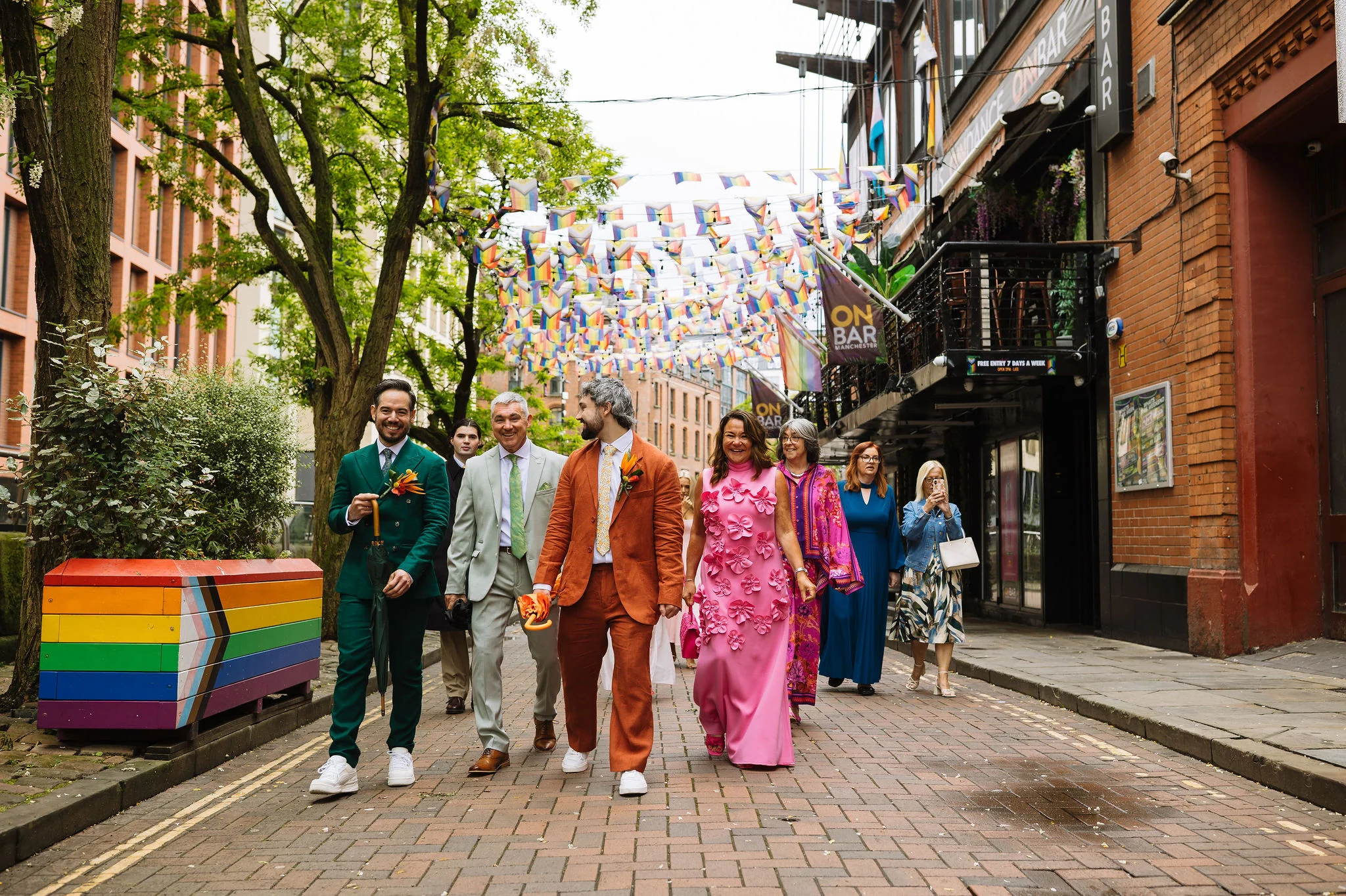 Two newlyweds walking with their wedding party beneath colourful flags
