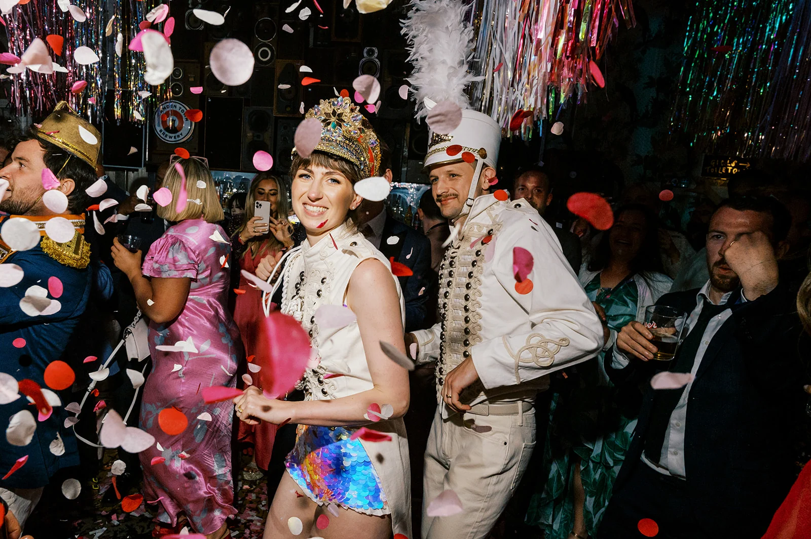 Rosalind and George in extraordinary hats celebrating amid falling petals