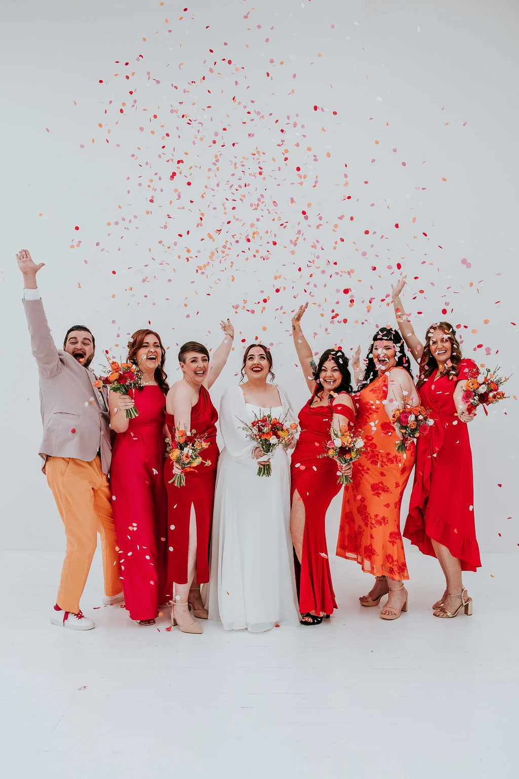 Olivia, Greg and their wedding party celebrating against a white backdrop