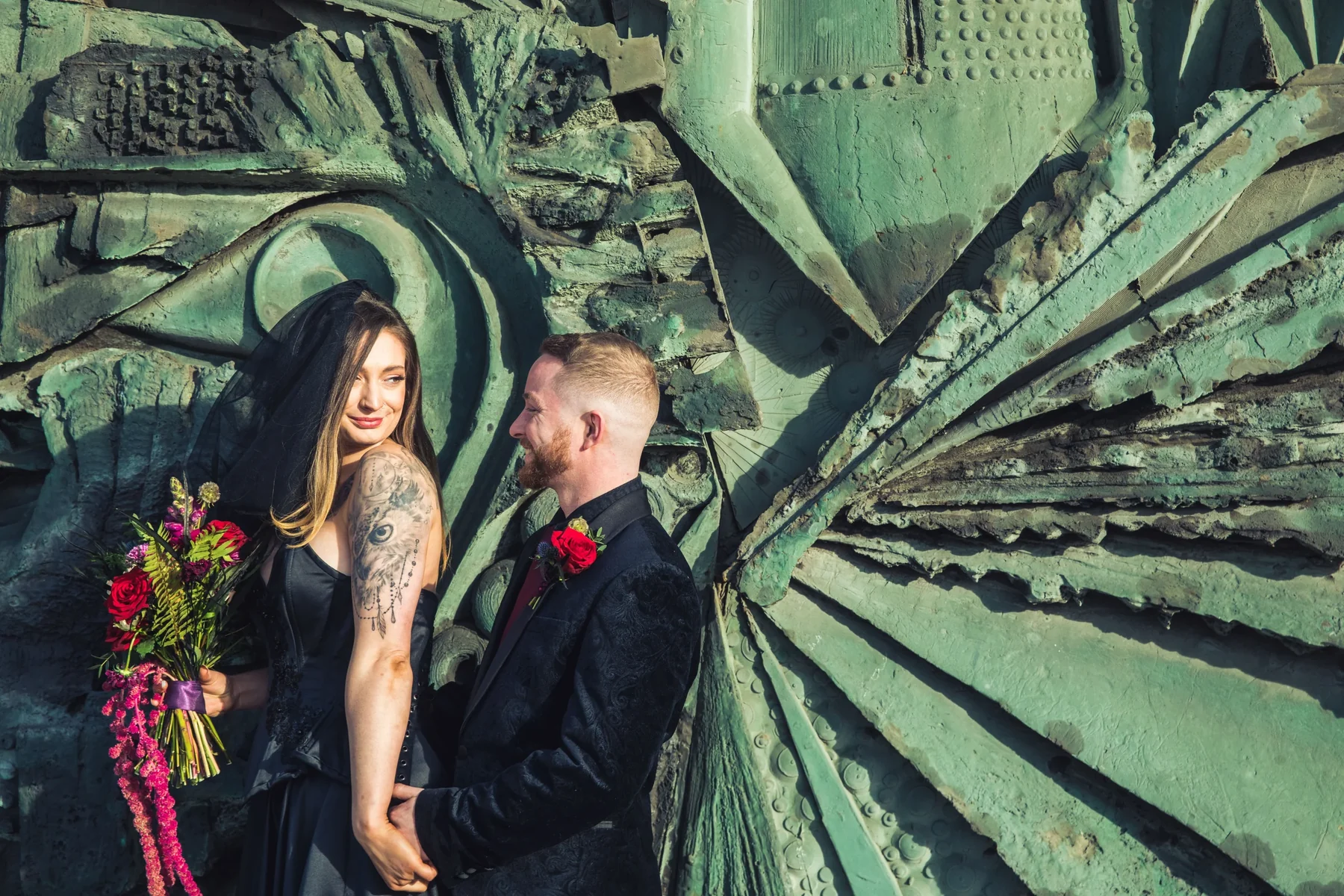 A tattooed couple standing against a textured blue stone wall